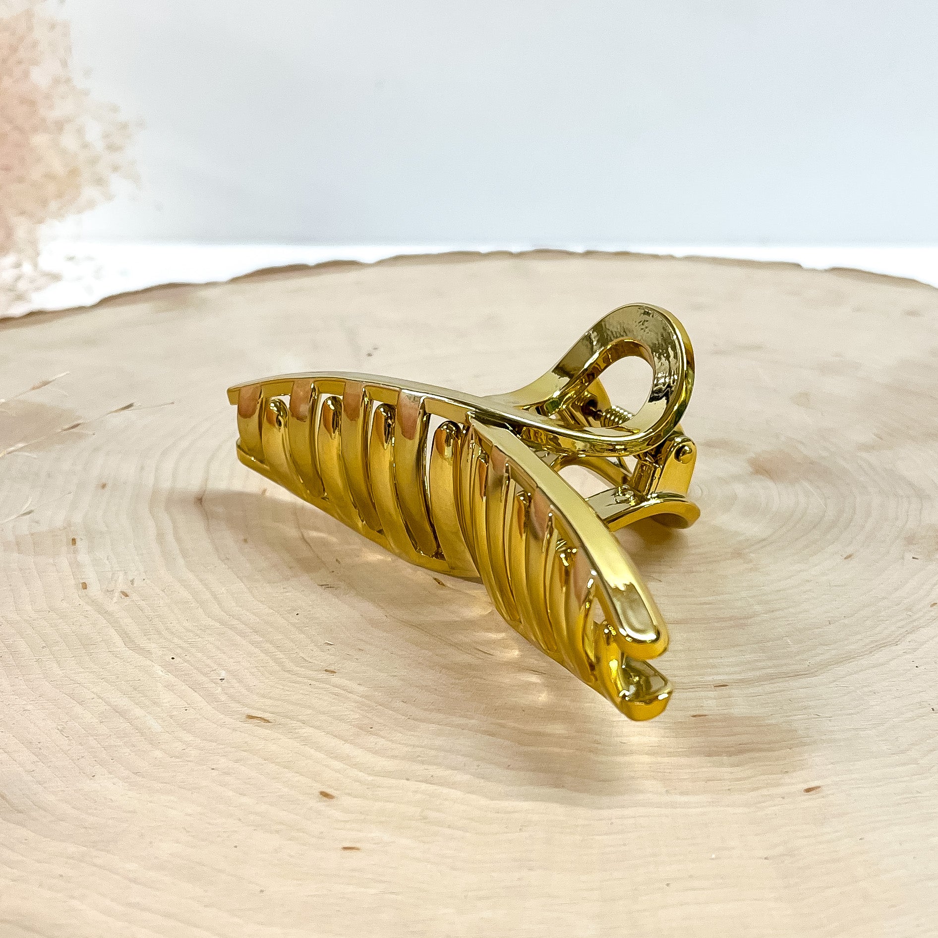 This is a long loop metallic hair clip in gold,  this clip is taken on a  slab of wood and in white background with a plant in the side as decor.