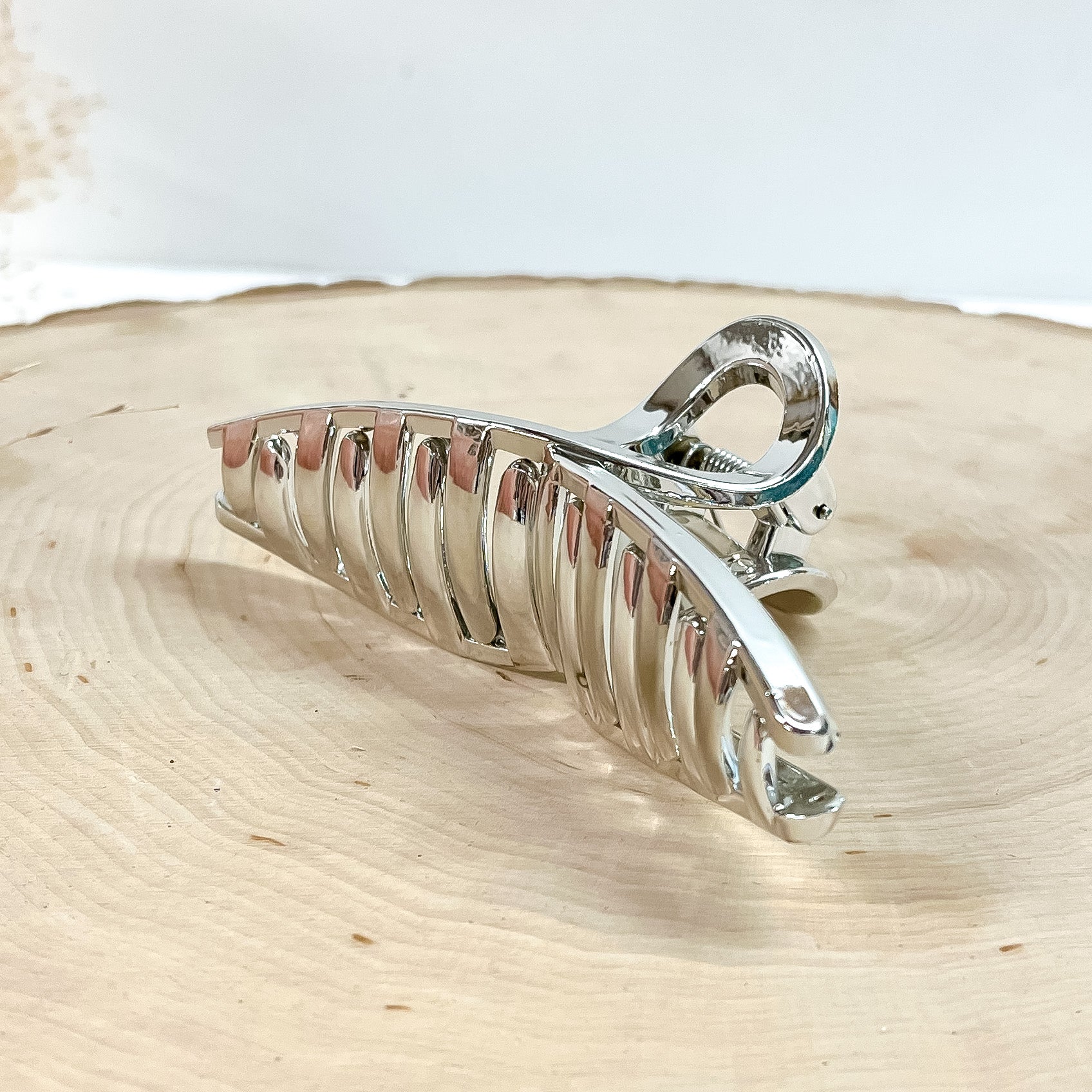 This is a long loop metallic hair clip in silver,  this clip is taken on a  slab of wood and in white background with a plant in the side as decor.