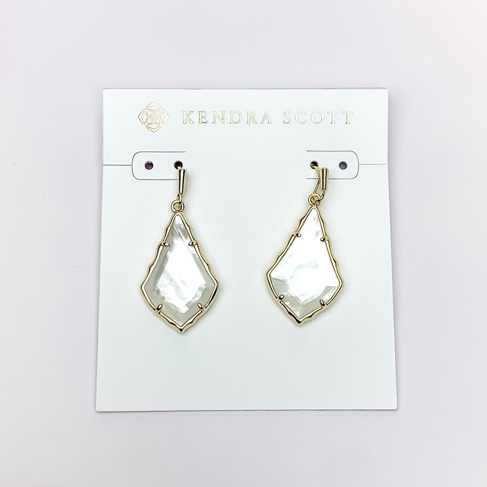 Gold outlien drop earrings with an ivory mother of pearl stone. These earrings are pictured on a white earrings holder on a white background. 