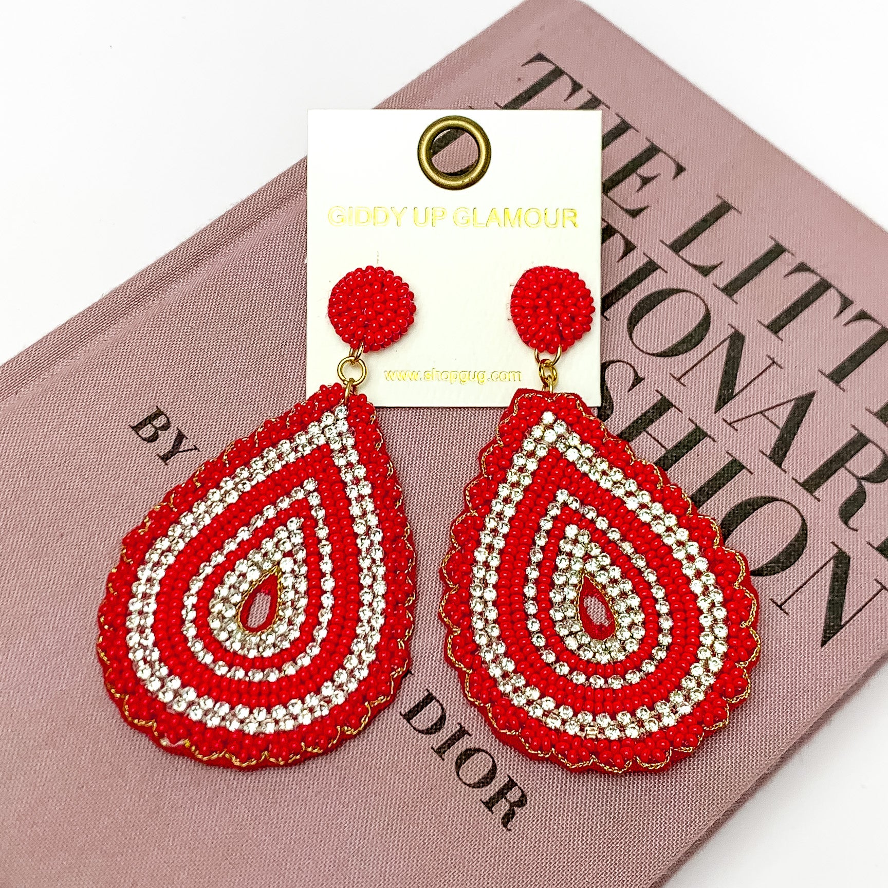 Sound Wave Beaded Drop Earrings with Clear Crystals in Red. Pictured on a white background with a book behind the earrings