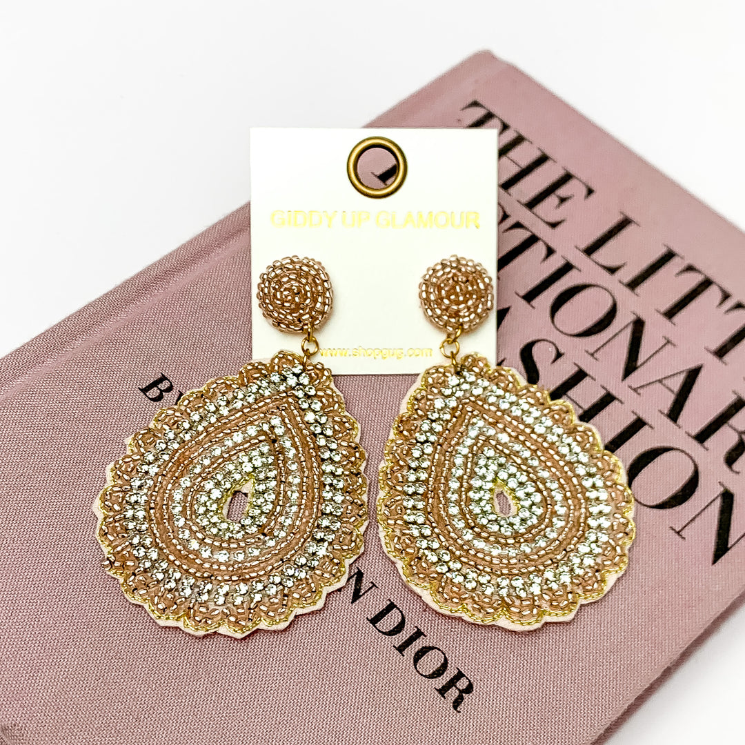 Sound Wave Beaded Drop Earrings with Clear Crystals in Champagne. Pictured on a white background with a book behind the earrings.