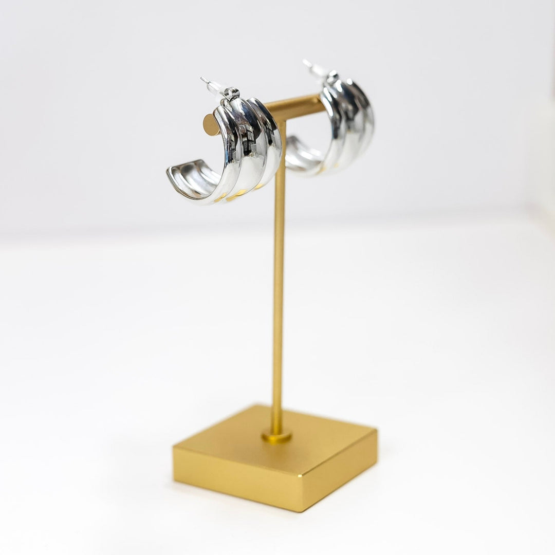 Pair of silver hoop earrings on a gold stand against a white background