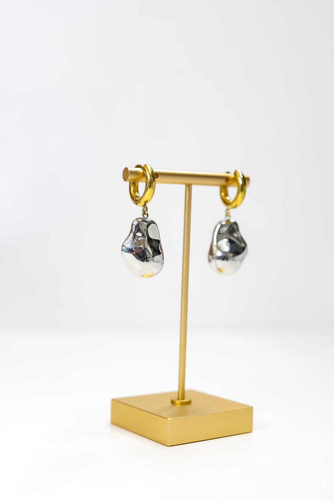 Gold earring stand with silver earrings on a white background
