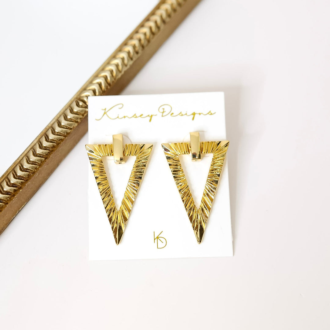 Gold triangle earrings on a white card with 'Kinsey Designs' branding, next to a gold decorative frame.