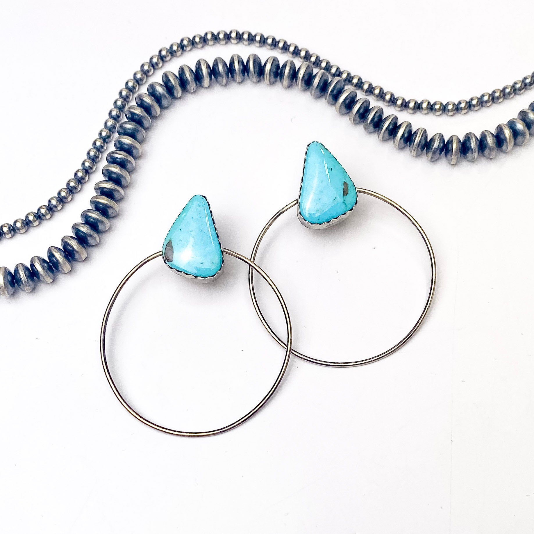 In the picture are handmade sterling silver hoops with a blue triangle stone stud on top with a white background