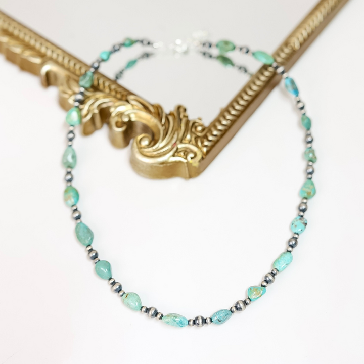 Handmade Red River Turquoise and Navajo Pearl necklace with sterling silver beads, displayed draped over an ornate gold frame.