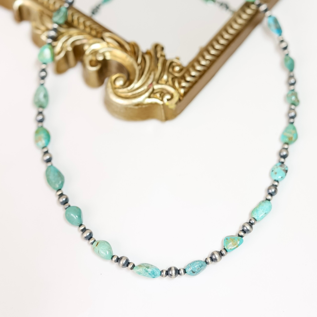 Handmade Red River Turquoise and Navajo Pearl necklace with sterling silver beads, displayed draped over an ornate gold frame.