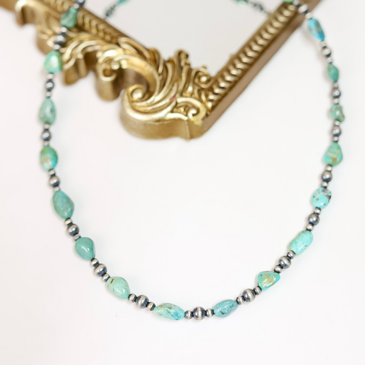 Handmade Red River Turquoise and Navajo Pearl necklace with sterling silver beads, displayed draped over an ornate gold frame.