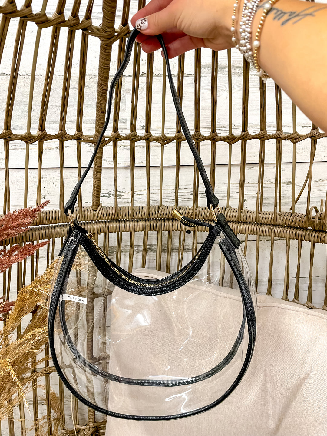 Clear handbag with black handle held by a hand against a textured wall background