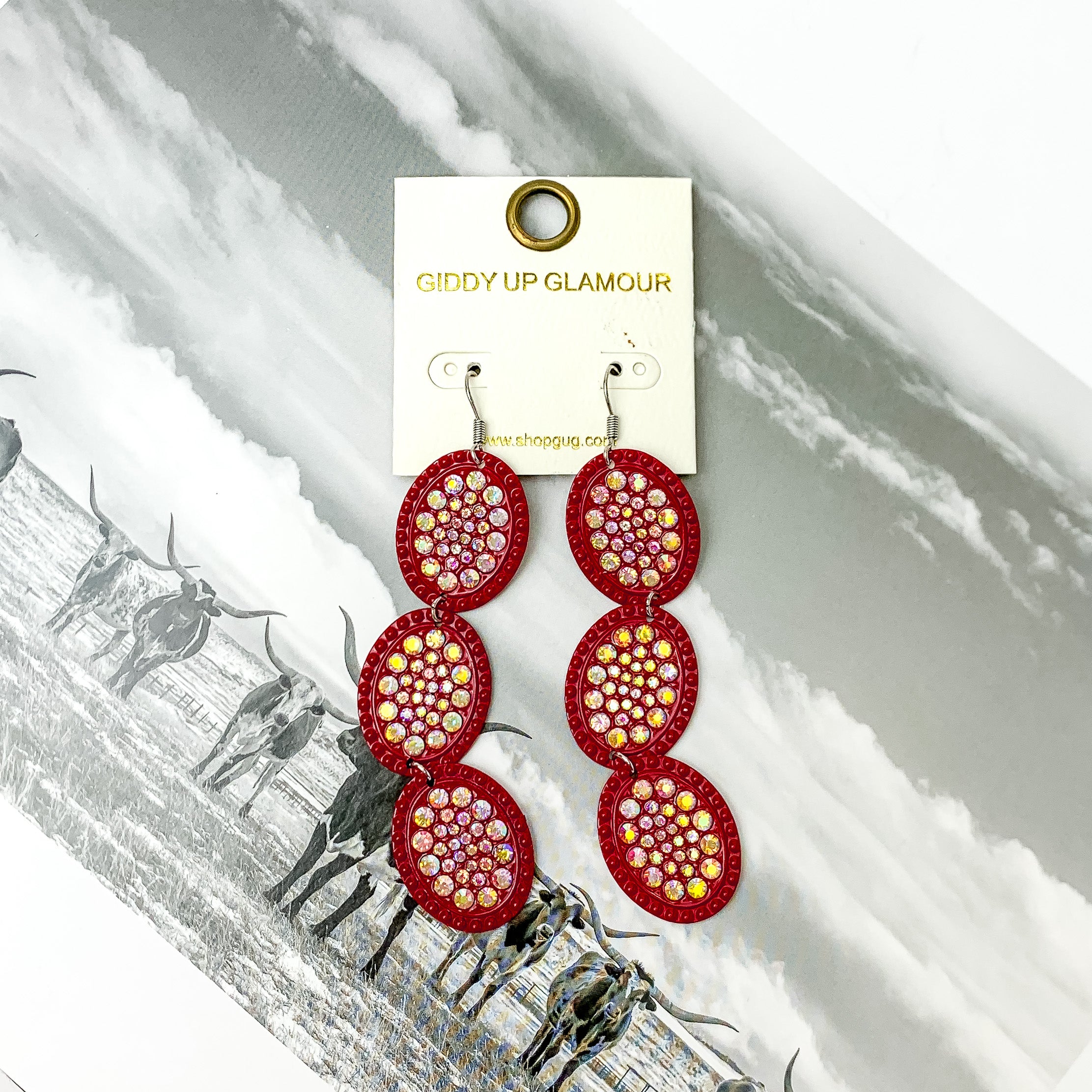 Three tier red with ab crystal oval shape dangle earrings with ab crystals. Pictured on a black and white western picture.