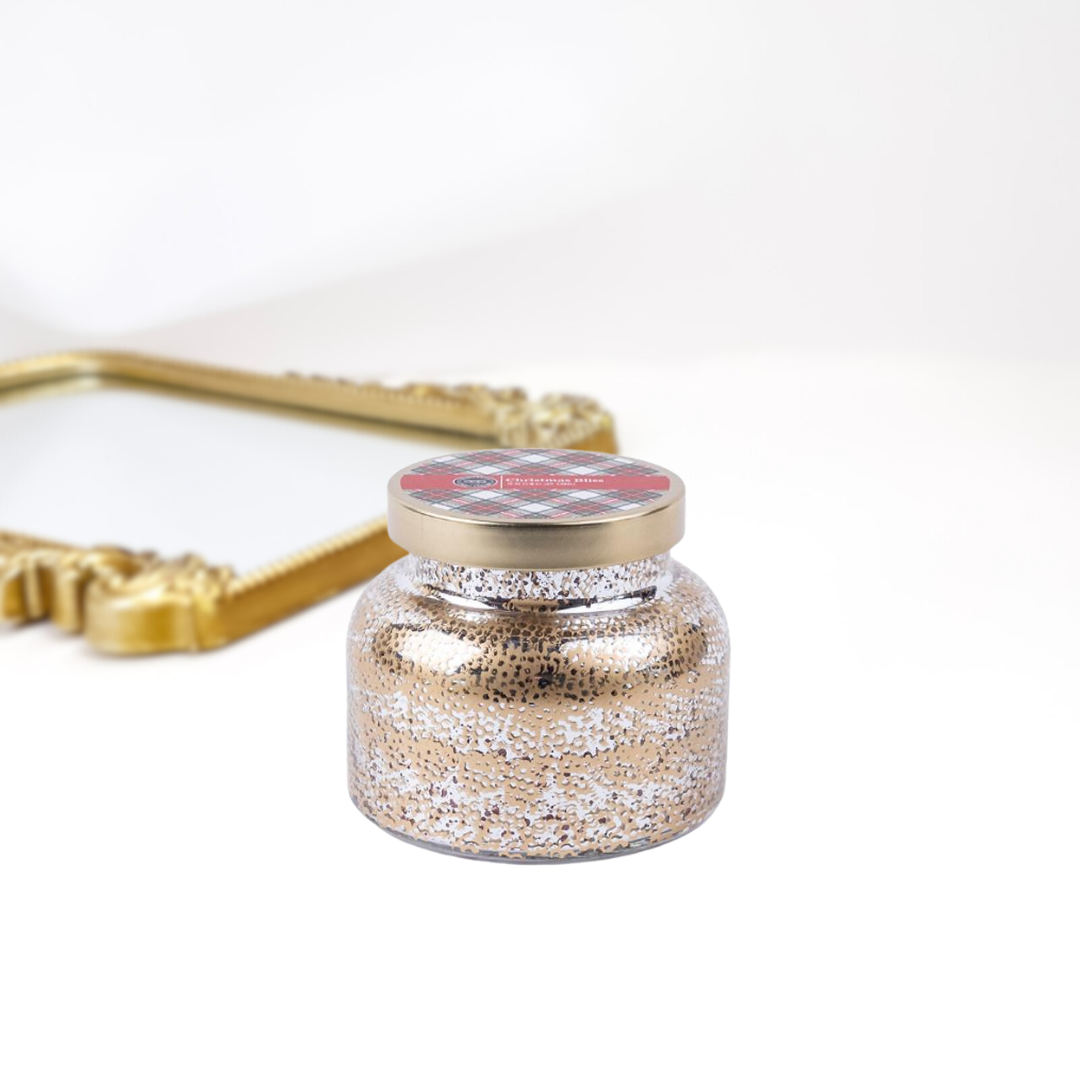 A solid white background with a gold mirror. A holiday inspired candle jar that is textured and has a gold lid.