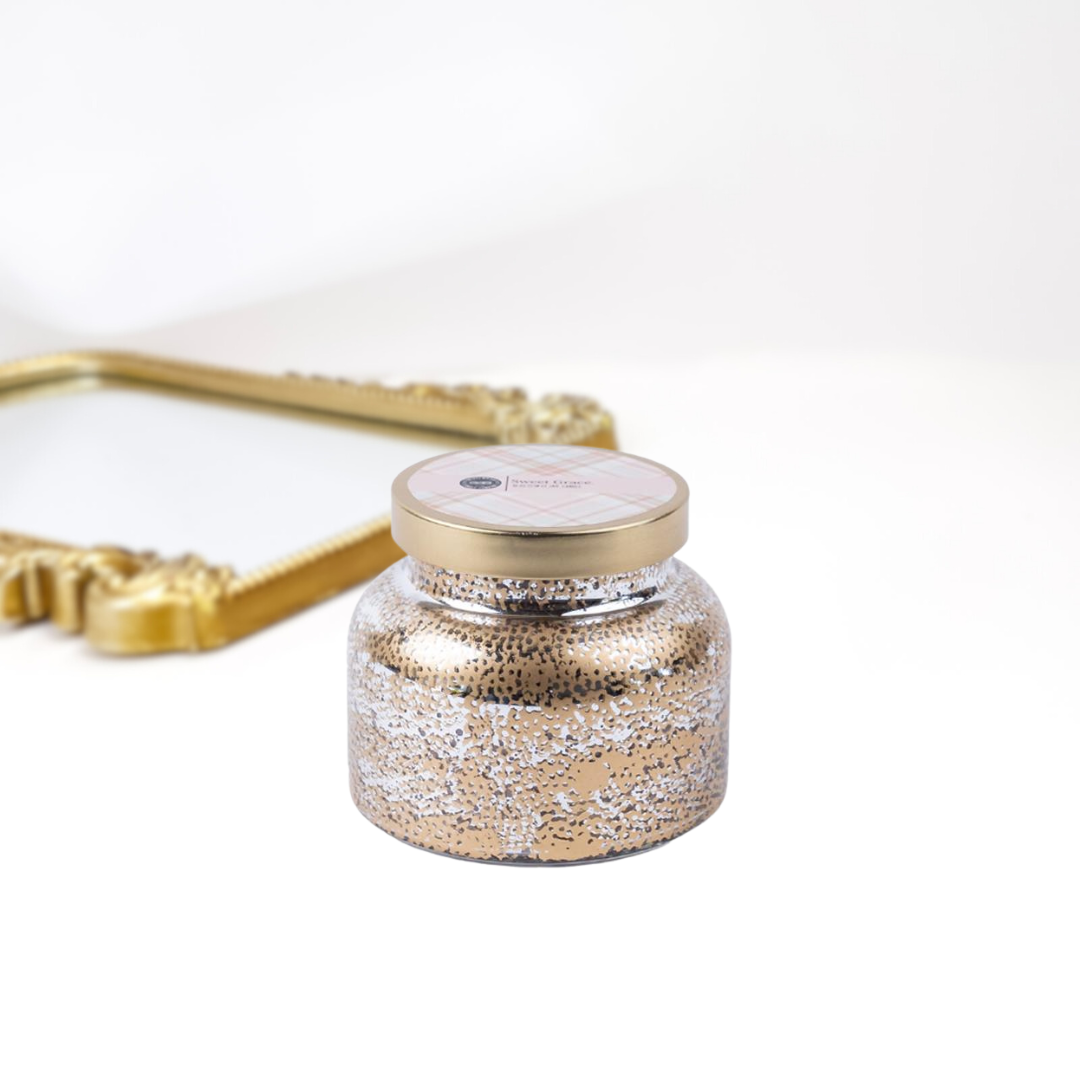 A solid white background with a gold mirror. A holiday inspired candle jar that is textured and has a gold lid.