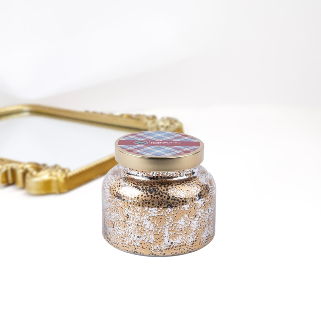 A solid white background with a gold mirror. A holiday inspired candle jar that is textured and has a gold lid.