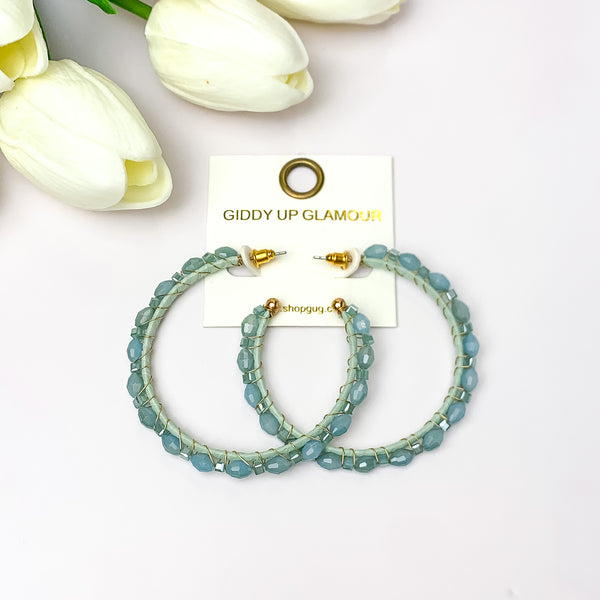 Large Hoops Outlined with Crystals in Aqua Blue. Pictured on a white background with white flowers in the top left.