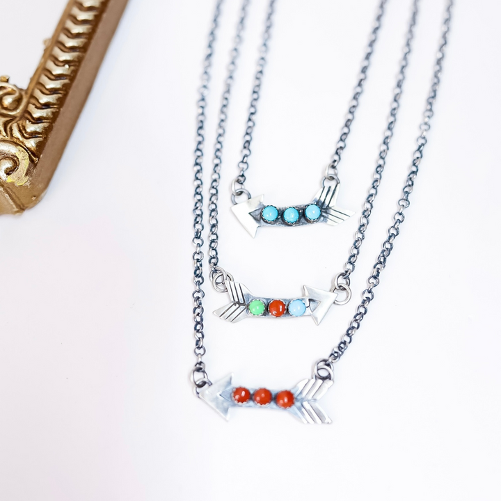 Three handmade Navajo arrow necklaces with turquoise, coral, and multi stone options, stamped by H. Tahe and E. Richards, displayed on silver chains.