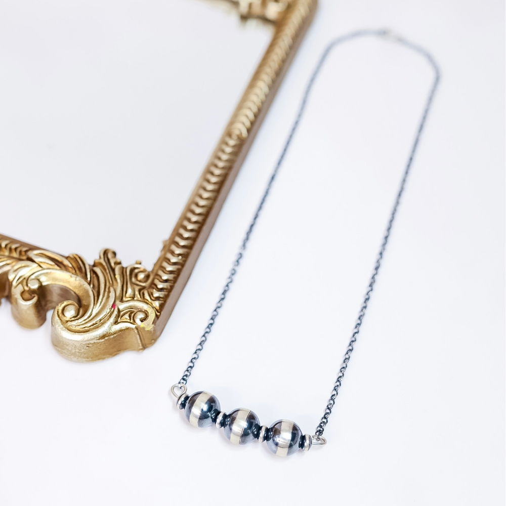 Close-up of Navajo Pearl Bar Necklace with 16mm sterling silver beads and saucer spacers on a 20-inch oxidized chain, styled flat with gold frame accent.