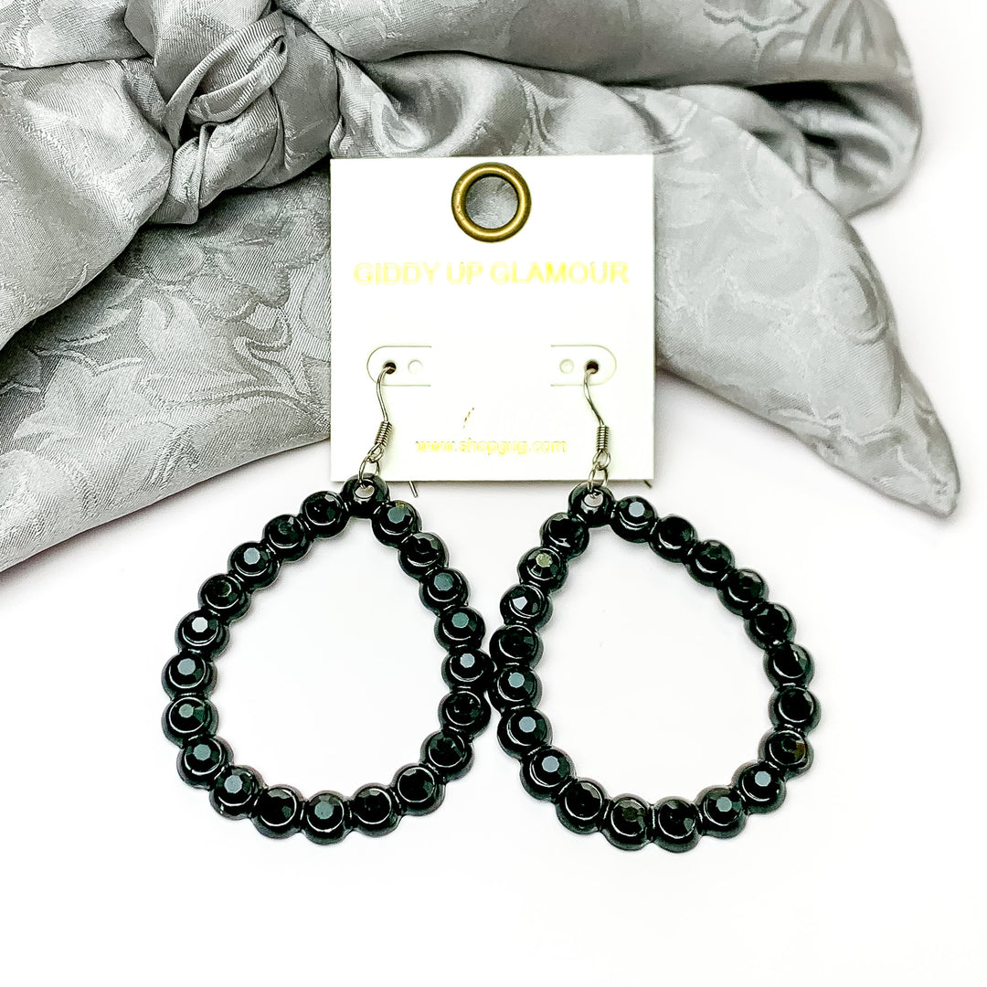 Open Teardrop Earrings with Black Crystal Outline in Black. Pictured on a white background with silver fabric at the top.