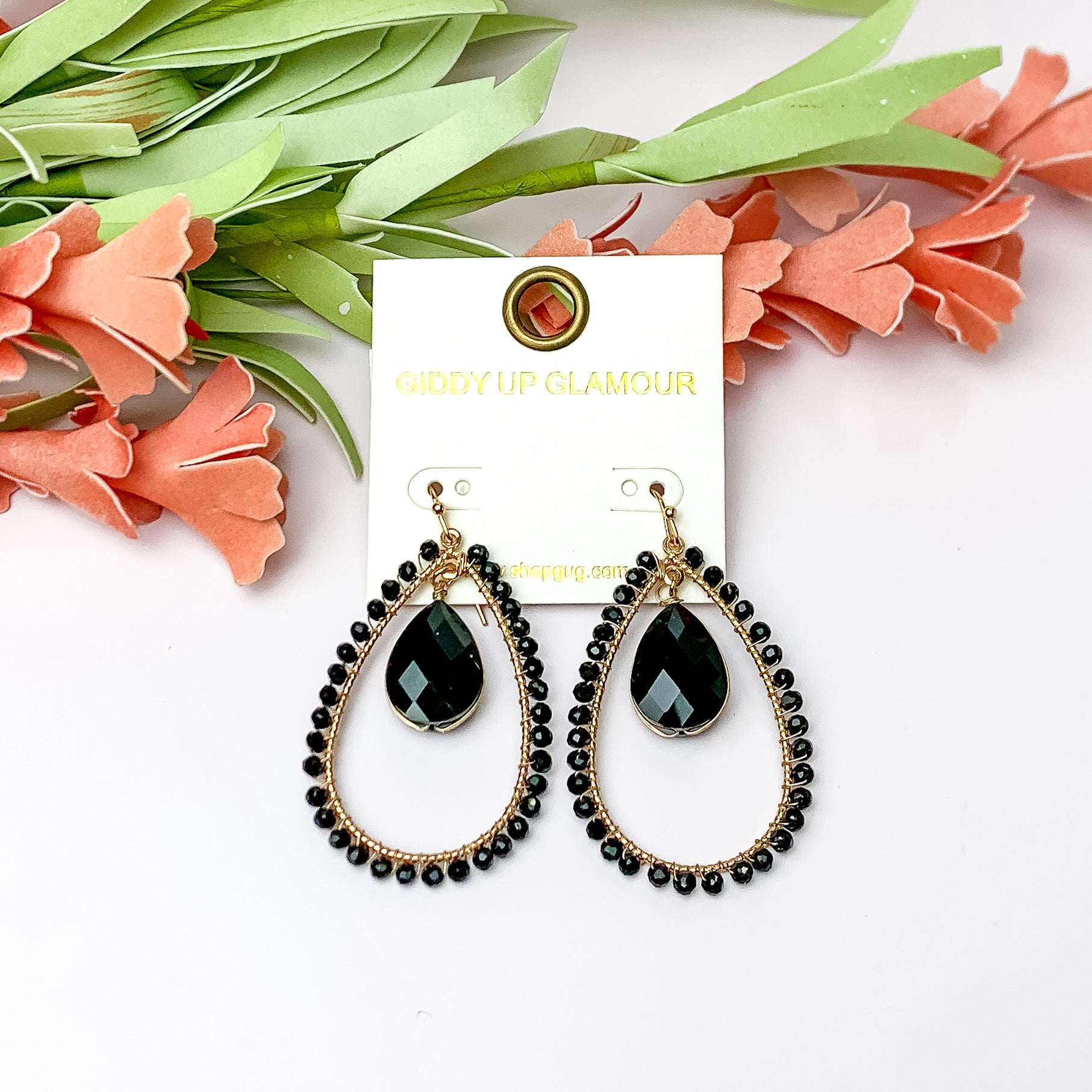 Black Stone Inside Open Beaded Teardrop Earrings with Gold Tone Outline. Pictured on a white background with flowers at the top.