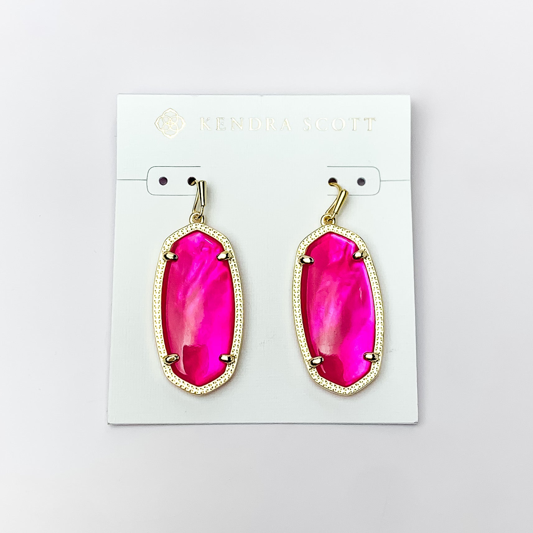 Gold oval drop earrings with a pink stone. These earrings are pictured on a white earring holder on a white background. 