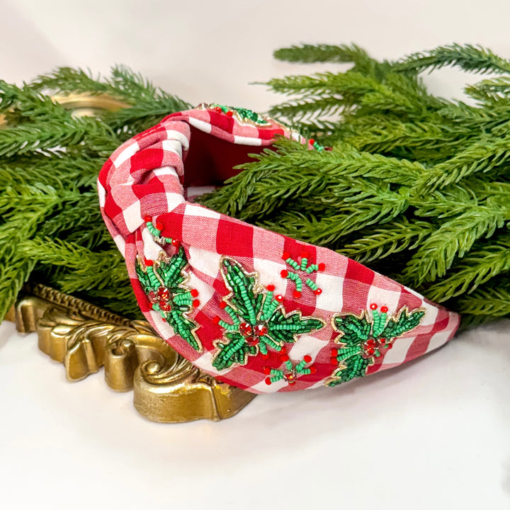 Red and white checkered headband with green embroidered holly design on a white background with greenery.