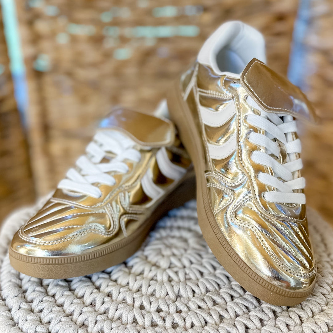 Gold and white sneakers on a textured stool with a wicker chair in the background