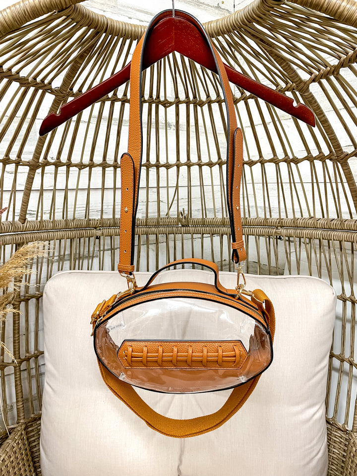 Brown handbag with clear front panel on a white cushion against a wicker background