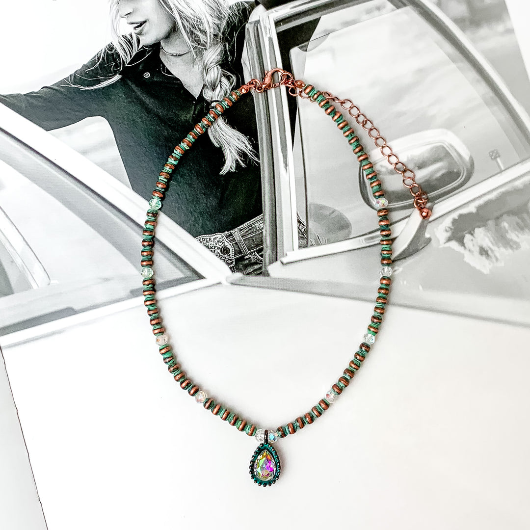 Patina short necklace with a crystal teardrop at the bottom. It does have small crystals through out the gold beads. The background is a black and white western photo.