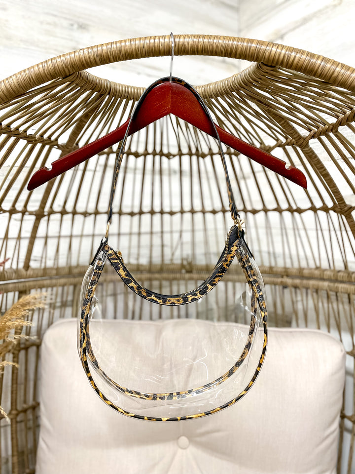 Clear stadium with leopard trim hanging from a wicker chair on a hanger. 
