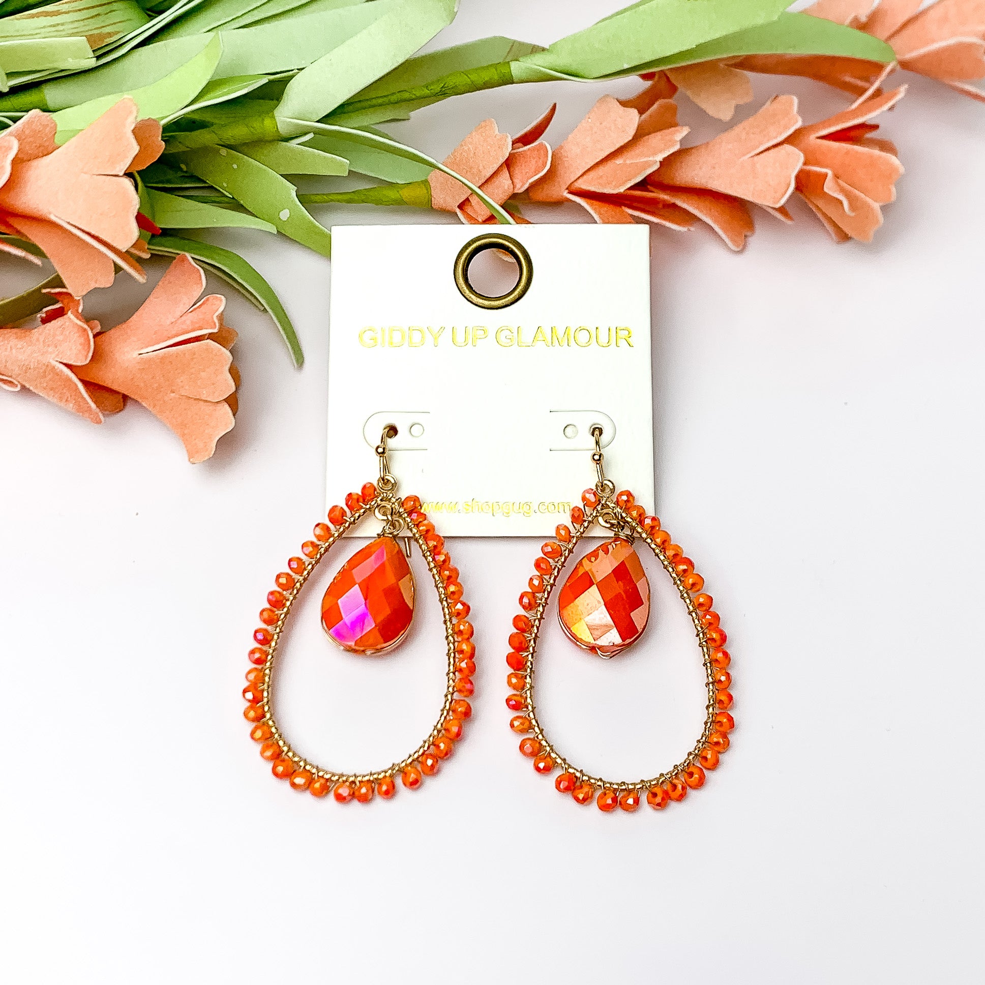 Orange Stone Inside Open Beaded Teardrop Earrings with Gold Tone Outline. Pictured on a white background with flowers at the top.