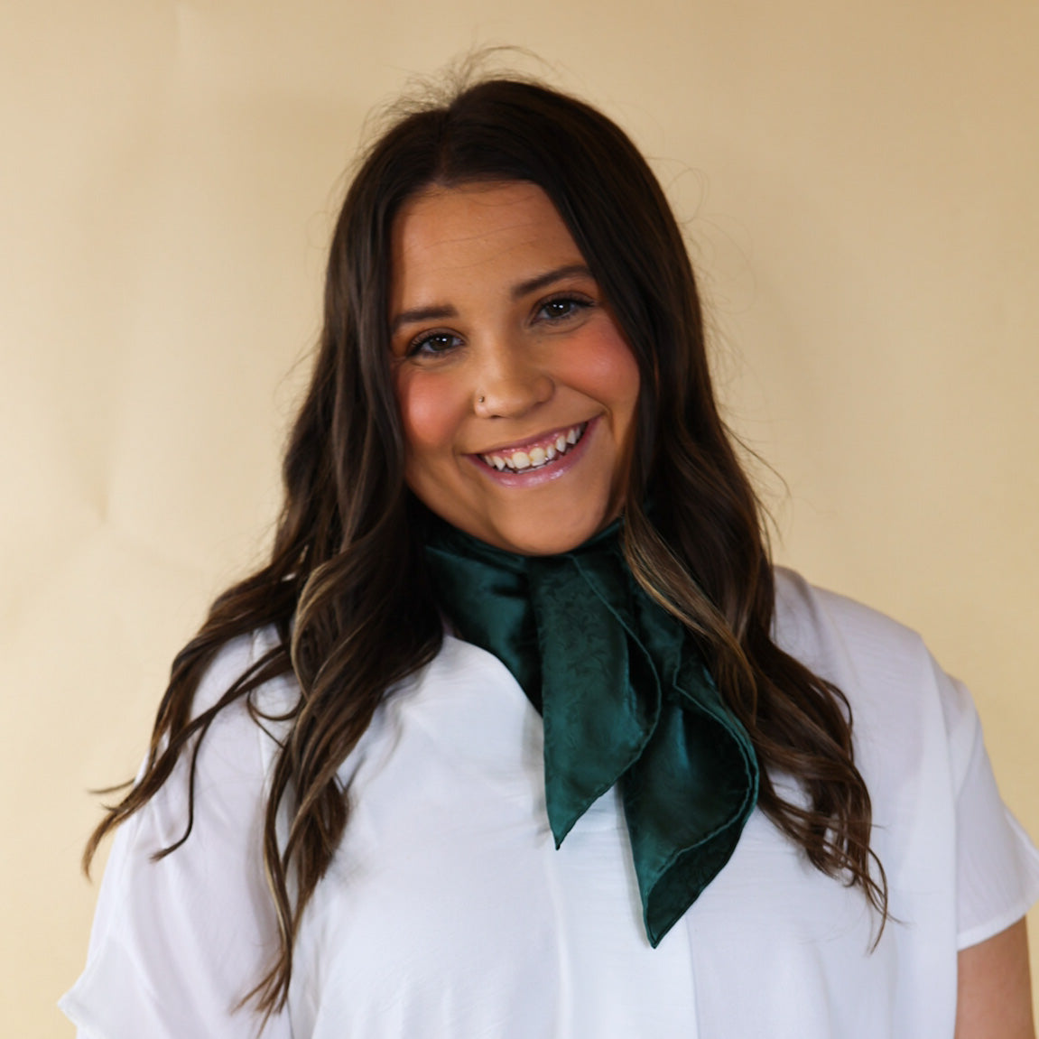 Brunette model wearing a short sleeve, denim button up with a eucalyptus green jacquard print scarf tied around her neck. This model is pictured in front of a beige background. 