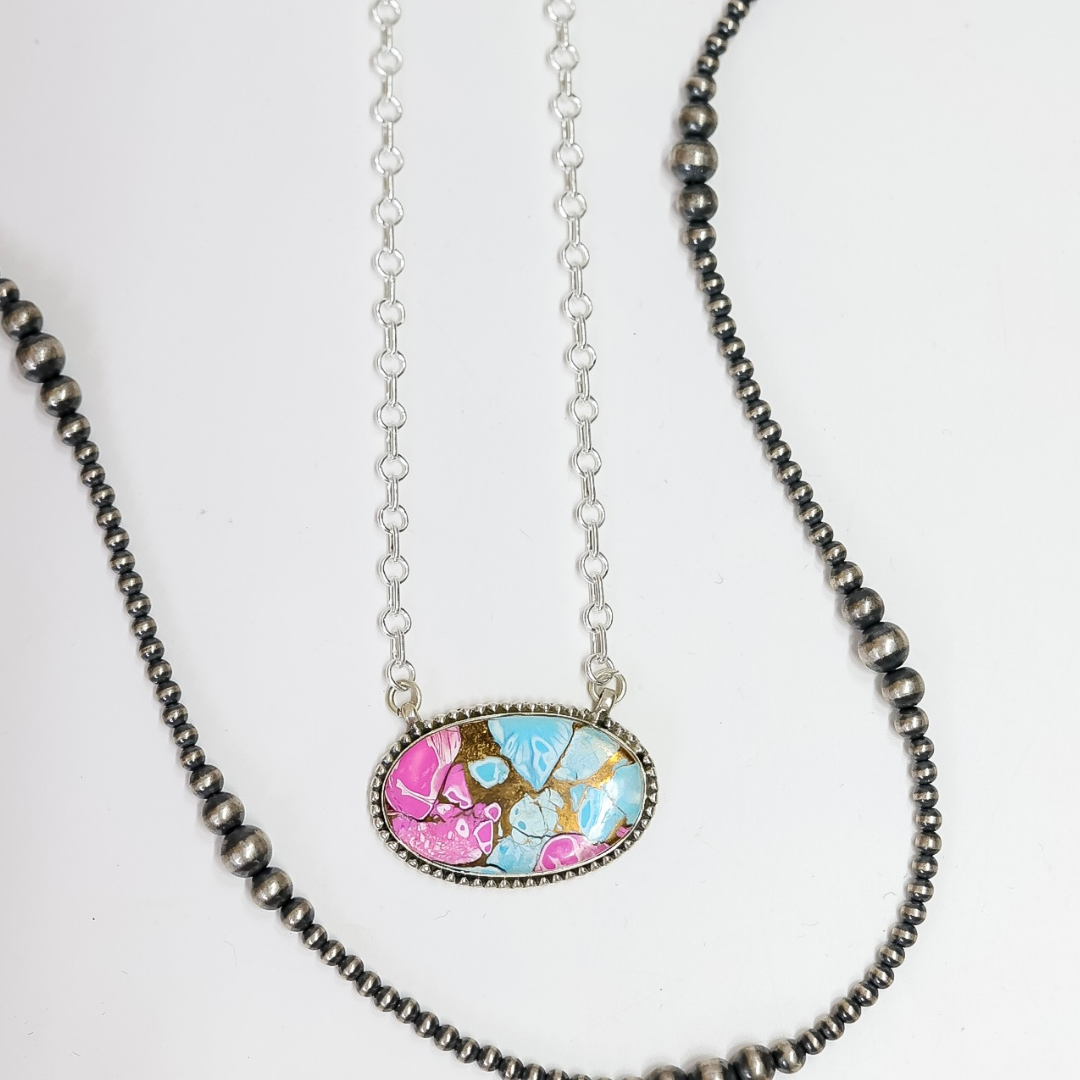 Close-up of a handmade oval necklace featuring hot pink and turquoise stone inlay with sterling silver rope detailing on an adjustable 20-inch chain.