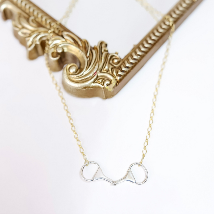 Gold necklace with a horse bit pendant on a white background