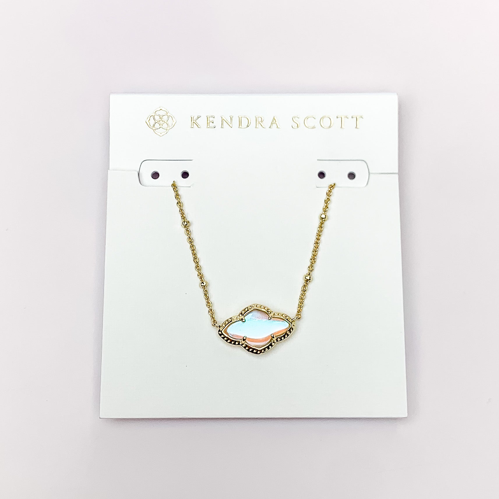 Gold chain necklace with a gold quatrefoil pendant and dichroic glass. This necklace is pictured on a white necklace holder on a white background. 