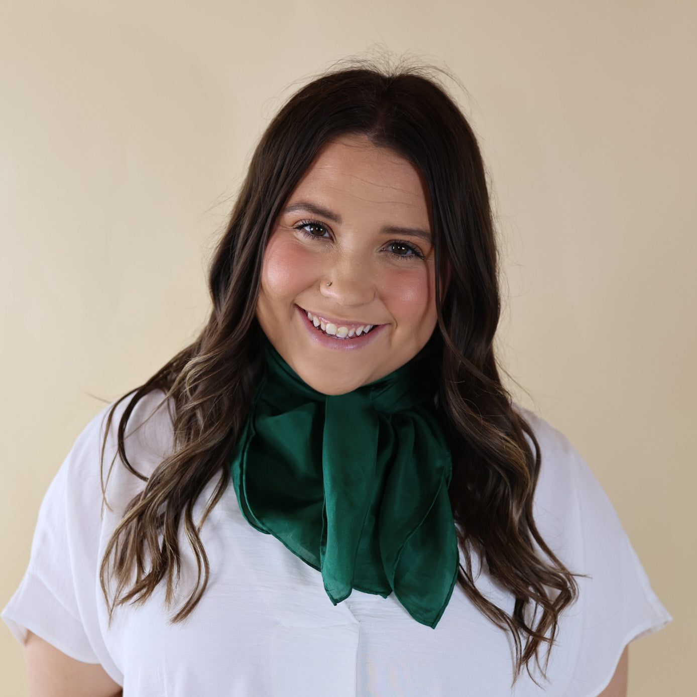Brunette model is pictured wearing a White, Drop shoulder top with a Solid Green scarf tied around her neck. Model is pictured in front of a beige background.