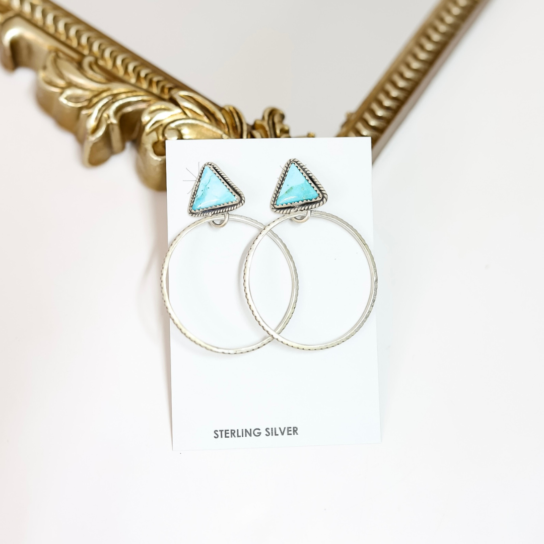 Pair of earrings with turquoise triangular stones on a white card with 'Sterling Silver' text, against a gold frame background.