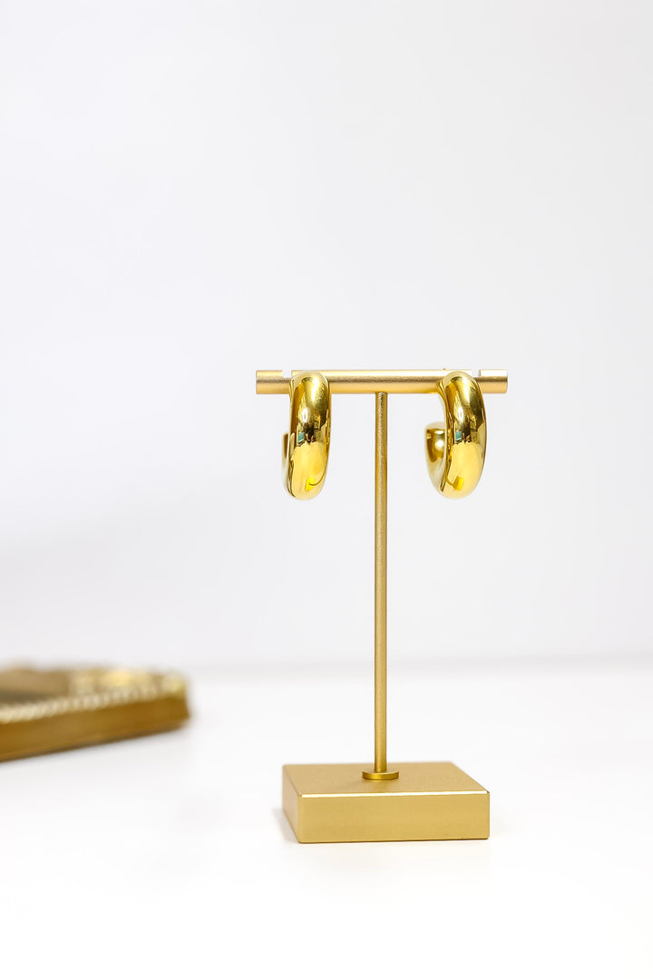 Gold hoop earrings on a matching gold stand against a white background