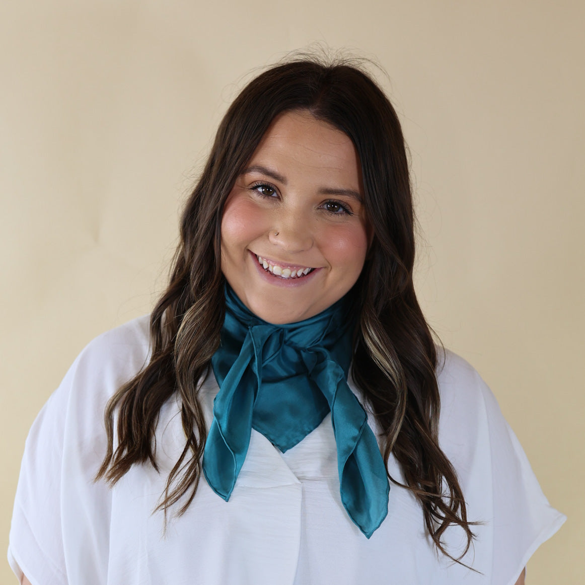 Brunette model is pictured wearing a white, Drop shoulder top with a Solid Blue scarf tied around her neck. Model is pictured in front of a beige background.