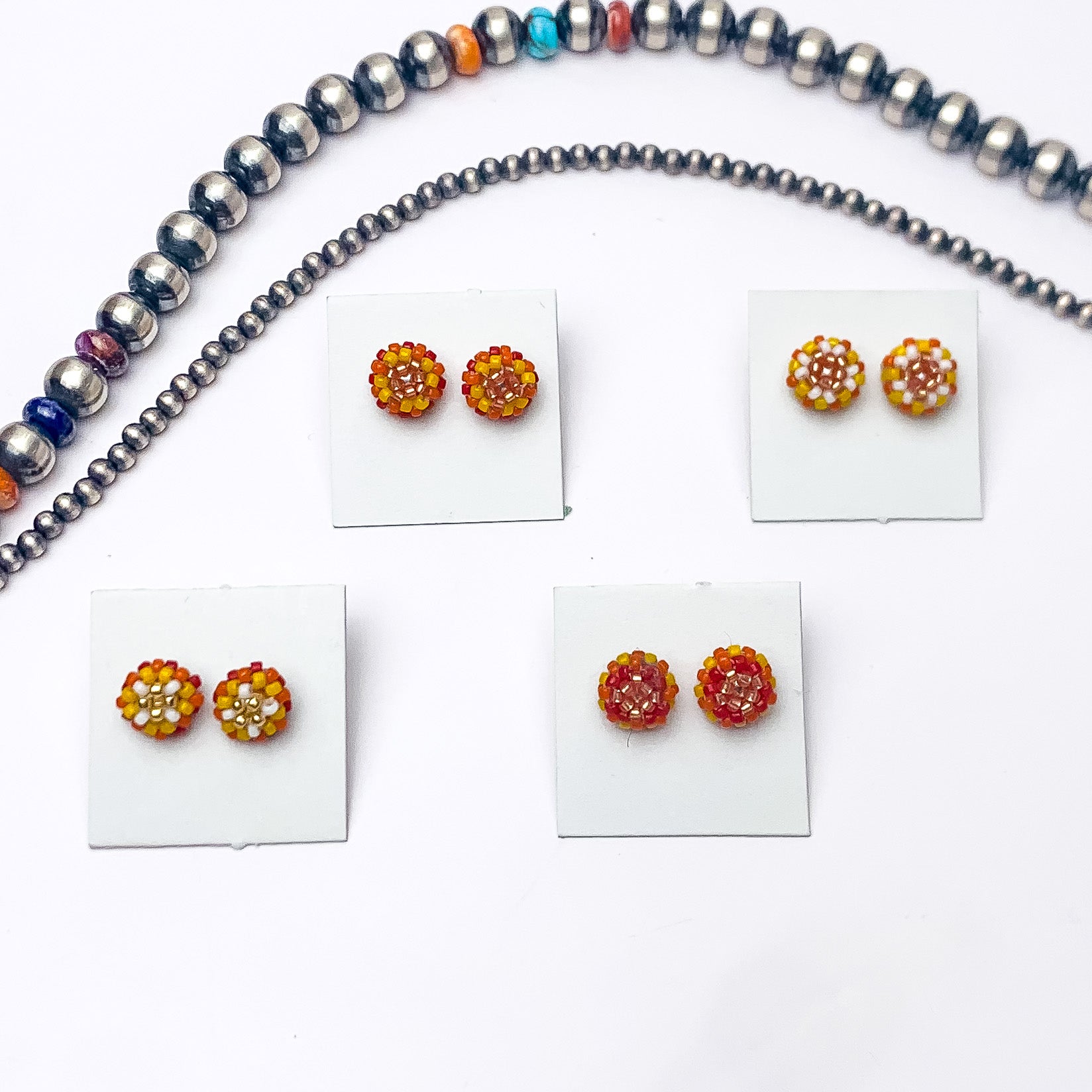 Pictured are four pairs of circle, beaded stud earrings in a mix of orange beads that are different in each pair. These earrings are pictured on a white background with silver beads above the studs. 