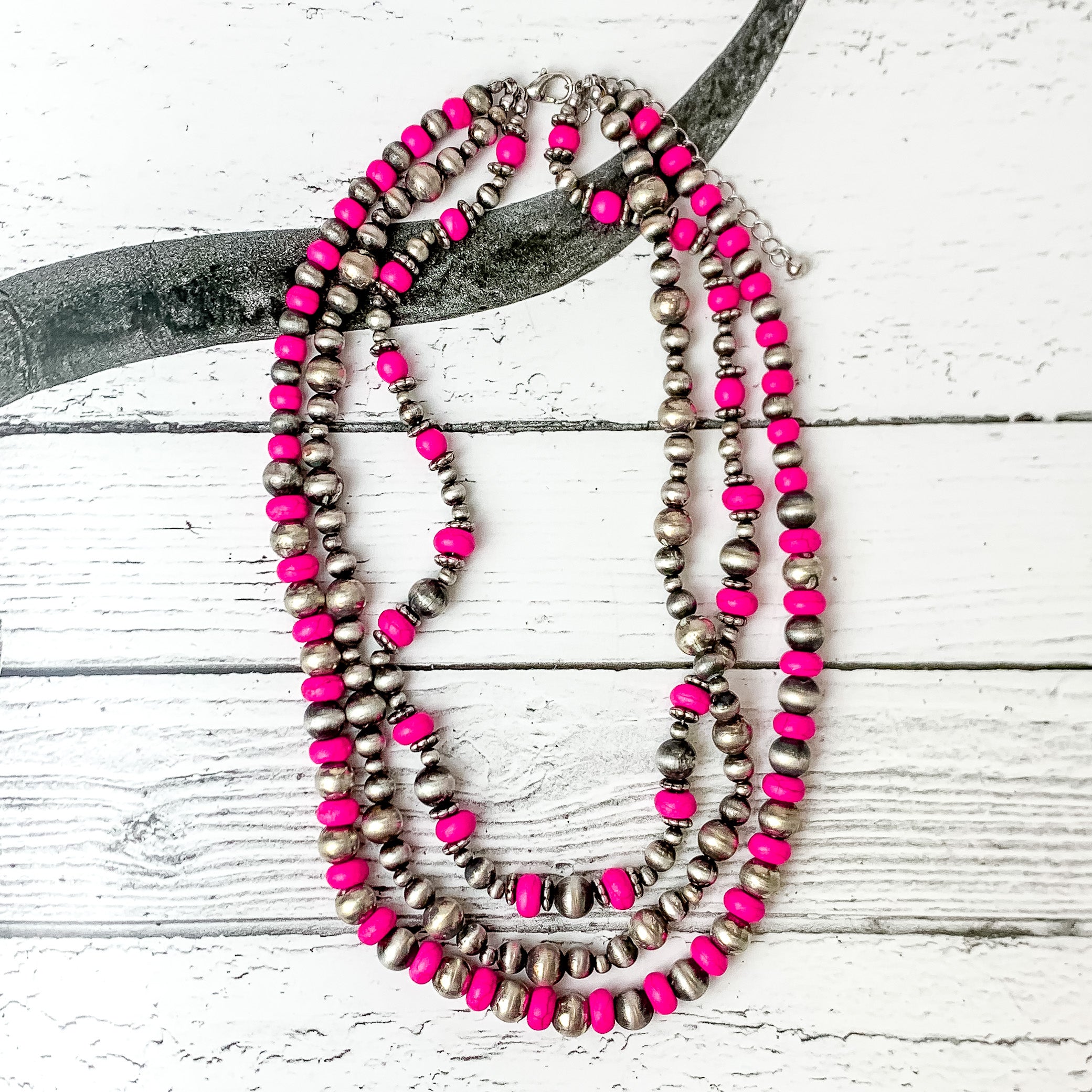 This necklace comes with three strands of beads. Two of them are mixed with fuchsia and faux navajo pearls in silver. The other strand is just faux navajo pearls in silver. Pictured on a black and white western photo in the background.