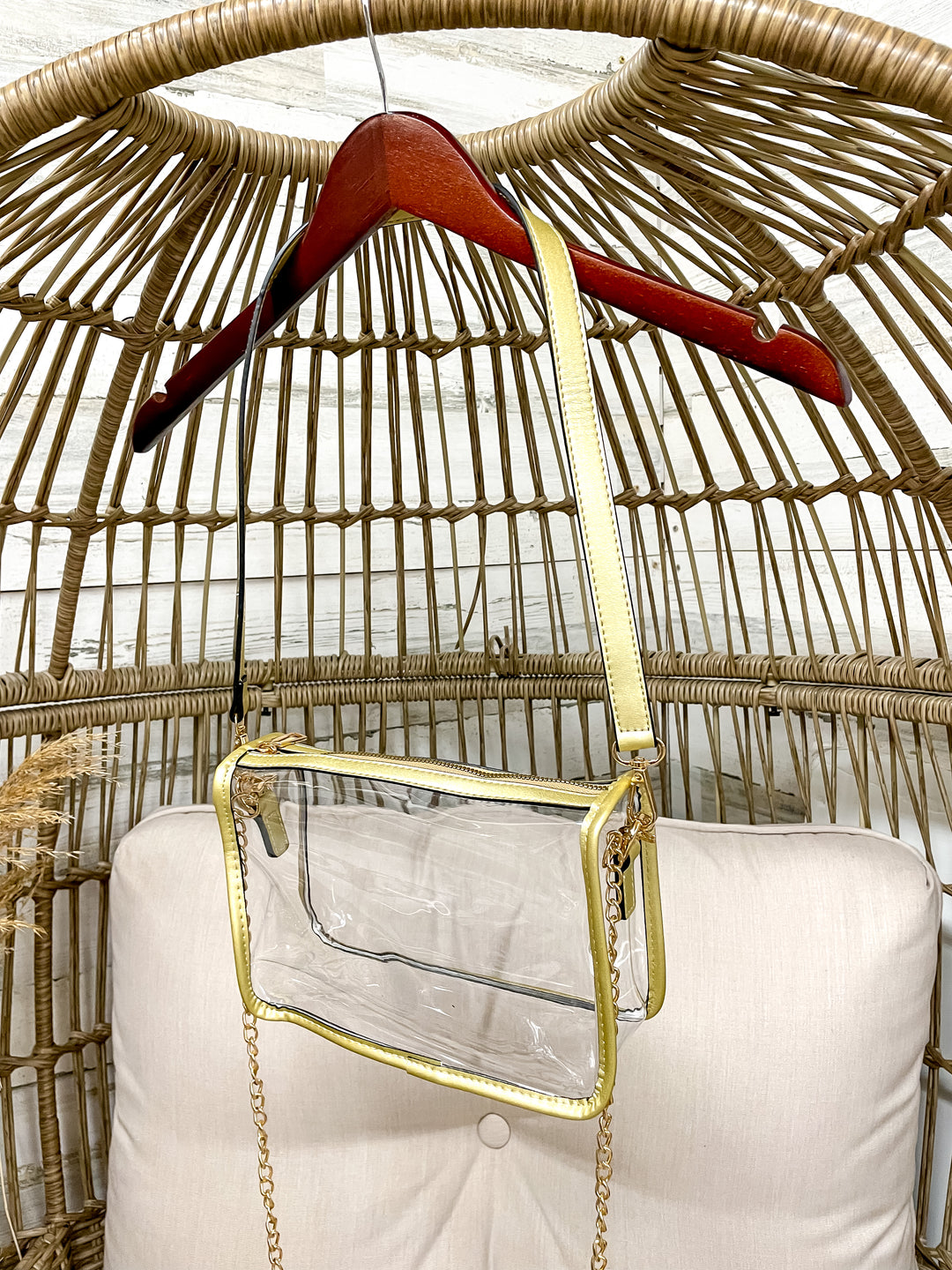 Clear handbag with gold chain detail on a wicker chair