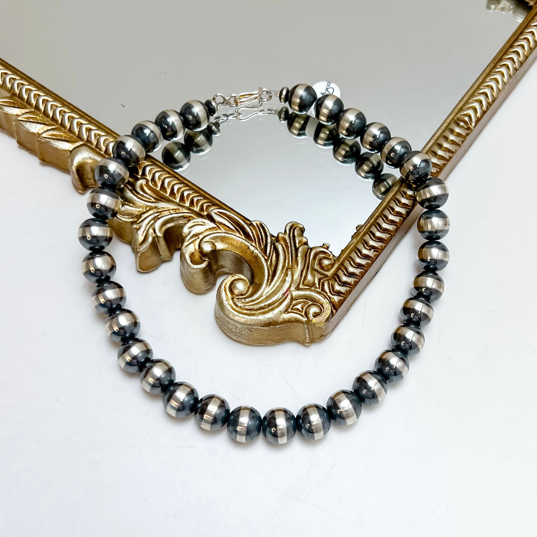 A hand strung sterling silver Navajo pearl necklace with large round beads, draped over an ornate gold mirror frame.