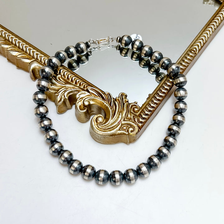 A hand strung sterling silver Navajo pearl necklace with large round beads, draped over an ornate gold mirror frame.