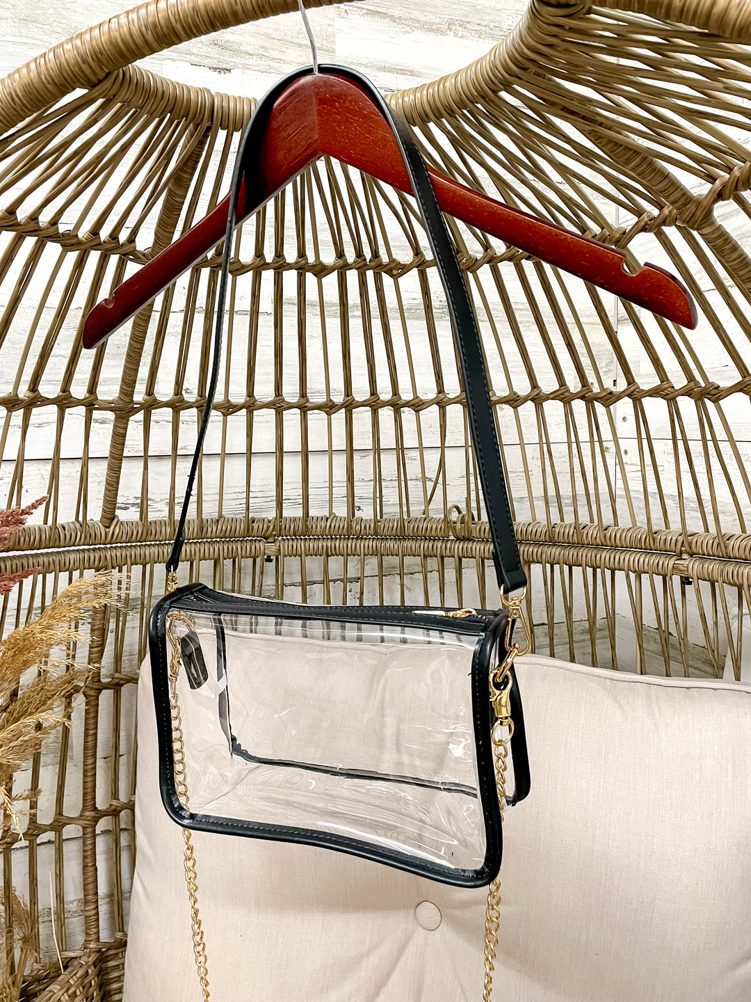 Clear handbag with black trim hanging on a red hanger against a wicker chair background