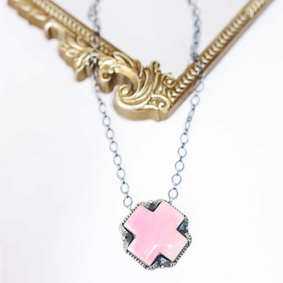 Sterling silver necklace with pink conch shell cross pendant handcrafted by Native American artist Tia Long, displayed on white background with ornate gold frame.