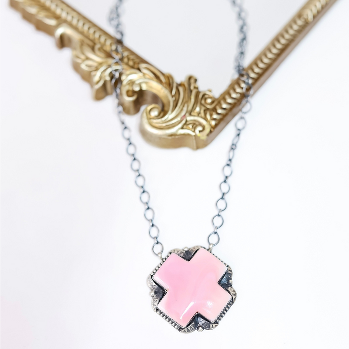 Sterling silver necklace with pink conch shell cross pendant handcrafted by Native American artist Tia Long, displayed on white background with ornate gold frame.