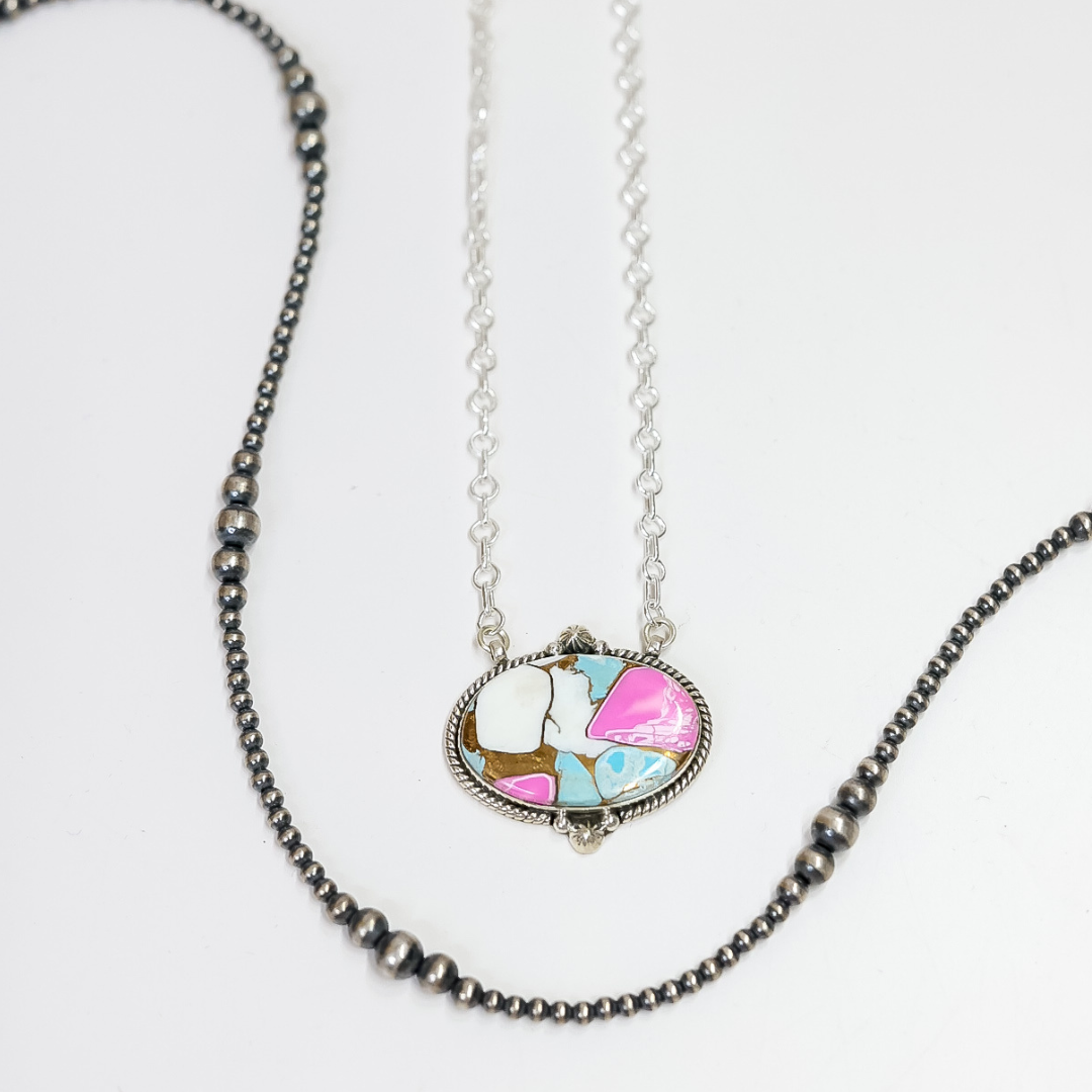 Close-up of a handmade oval necklace featuring hot pink and turquoise stone inlay with sterling silver rope detailing on an adjustable 20-inch chain.