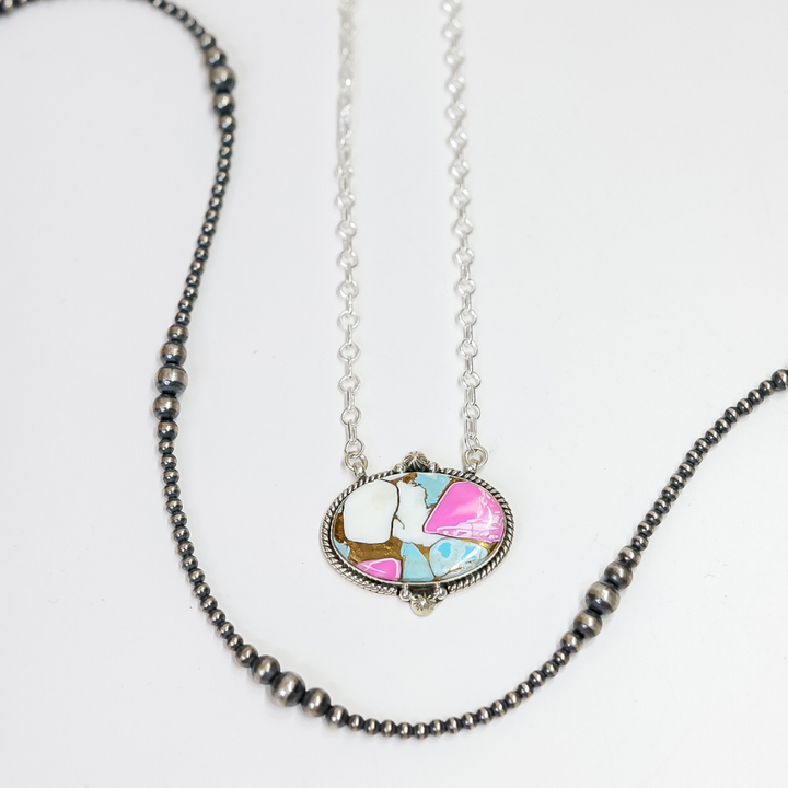 Close-up of a handmade oval necklace featuring hot pink and turquoise stone inlay with sterling silver rope detailing on an adjustable 20-inch chain.