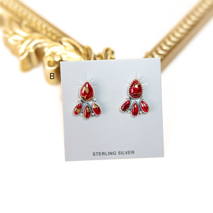 Red earrings on a white card with 'Sterling Silver' text, gold necklace in background