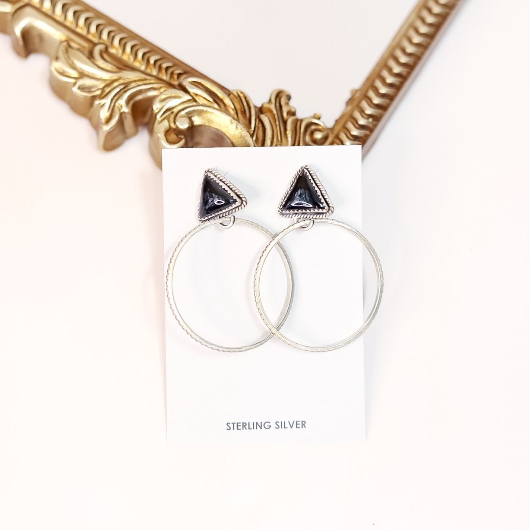 Sterling silver hoop earrings with black onyx triangle studs, handmade and stamped HaDa, styled on a white card with gold accent mirror in background.