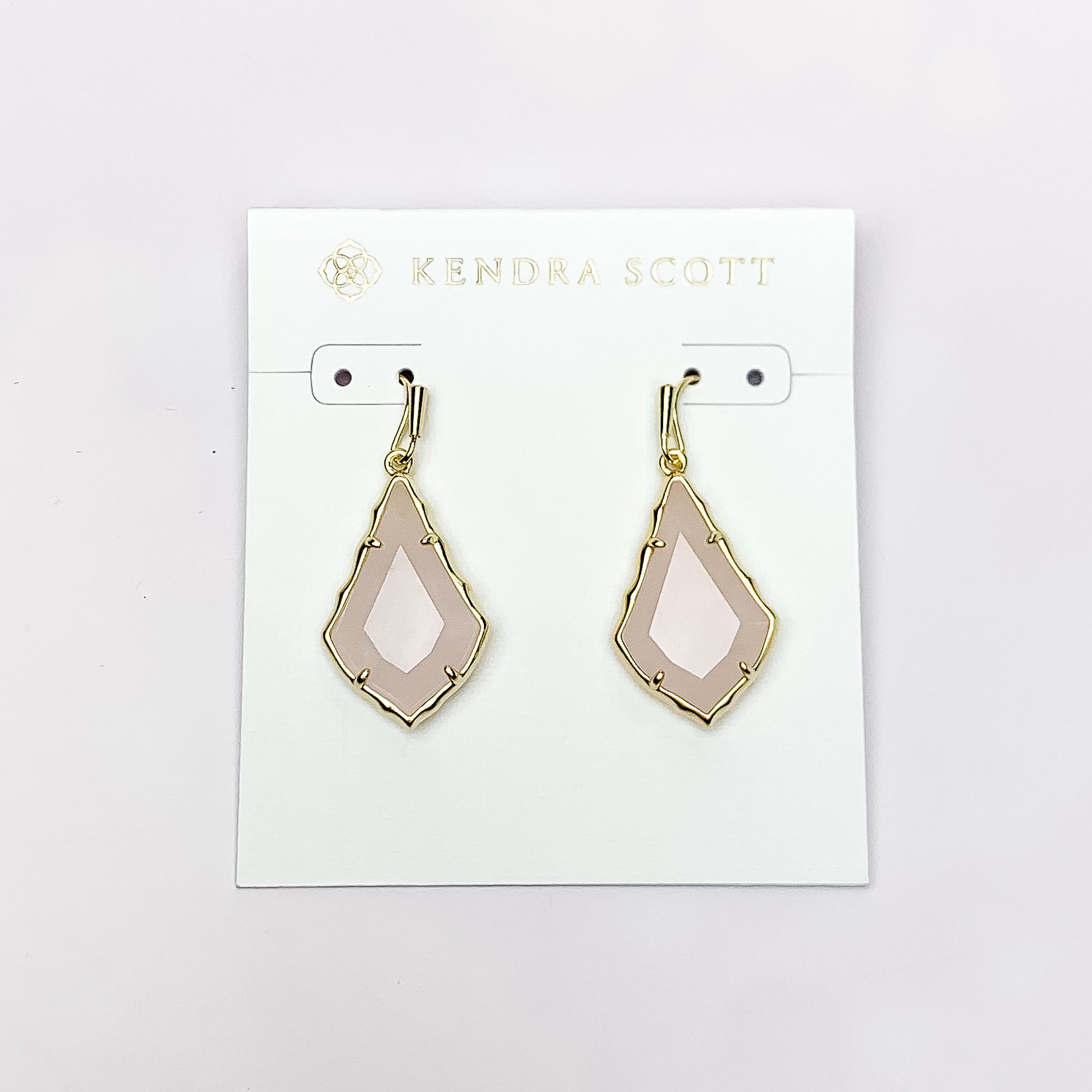 Gold outlien drop earrings with a rose quartz stone. These earrings are pictured on a white earrings holder on a white background. 